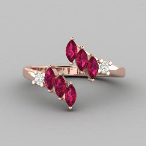May include: Rose gold ring featuring marquise-cut ruby gemstones and round-cut diamonds. The ring has a bypass design with the gemstones arranged in a flowing, asymmetrical pattern. The ring's band is a polished rose gold.