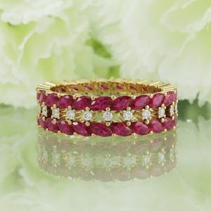 Op de afbeelding: Een gouden ring met rijen marquise-geslepen robijnen en kleine, ronde diamanten. Het ontwerp van de ring omvat drie rijen edelstenen, waarbij de robijnen het belangrijkste patroon vormen en de diamanten accenten toevoegen.