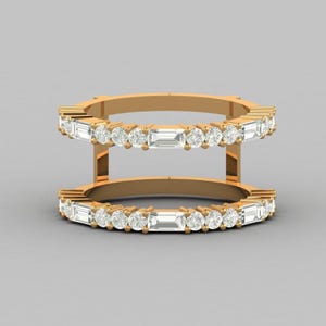 May include: A double-band gold ring featuring two parallel rows of alternating round-cut and baguette-cut clear stones. The bands are connected by vertical gold bars, creating a structured, open-frame design with a polished metallic finish.