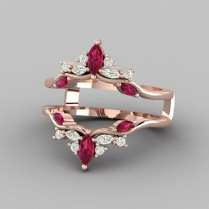 May include: Rose gold ring with a distinctive design. The ring features marquise-cut ruby-red gemstones and small, round, clear gemstones. The ring has a double band design, with the top band curving over the bottom band.
