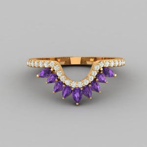 Puede incluir: Un anillo dorado con un diseño curvo. El anillo presenta una fila de pequeñas piedras preciosas transparentes a lo largo de la curva superior y una serie de piedras preciosas moradas en forma de lágrima debajo. El anillo está sobre un fondo gris.