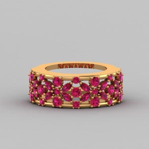 Op de afbeelding: Een gouden ring met een herhalend bloemmotief, bezet met talloze ronde en marquise-geslepen felroze edelstenen. Het ontwerp bestaat uit onderling verbonden metalen segmenten die de stenen in een open structuur op hun plaats houden.