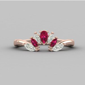 May include: A rose gold ring with a floral design. It features pear-shaped red gemstones and marquise-cut white gemstones. The ring's band has a twisted design, and the gemstones are set in a crown-like arrangement.