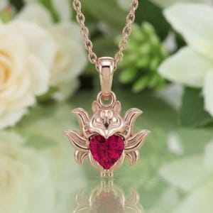 Puede incluir: Collar con colgante de oro rosa con una piedra preciosa roja rubí en forma de corazón. El colgante tiene un diseño ornamentado con un motivo floral o animal estilizado. La cadena del collar también es de oro rosa.