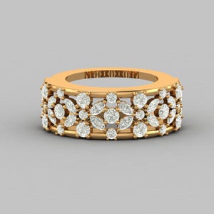 Pode incluir: Um anel dourado com um design floral. O anel é incrustado com numerosas pedras preciosas transparentes de corte redondo e marquesa. A banda tem um padrão repetitivo de trabalho aberto e pedras preciosas. O anel está sobre um fundo cinza neutro.