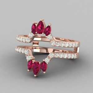 Peut inclure: Bague en or rose avec un design à double bande. La bande supérieure présente trois pierres précieuses rouges profondes en forme de poire et une rangée de petites pierres précieuses claires. La bande inférieure a un design similaire.