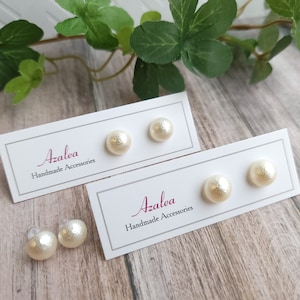 May include: Two pairs of white pearl stud earrings displayed on white cards with the text "Azalea Handmade Accessories".