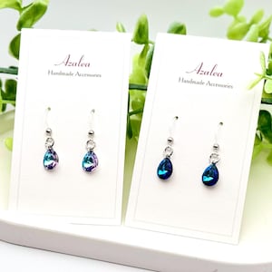 May include: Two pairs of teardrop-shaped earrings with silver posts. The earrings on the left are iridescent blue and purple. The earrings on the right are a deep blue color. The earrings are displayed on white cards with the text "Azalea Handmade Accessories".