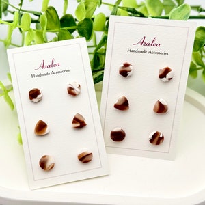 May include: Two cards with the text "Azalea Handmade Accessories" and a display of six brown and white marbled earrings. The earrings are in the shapes of a circle, triangle, and pentagon.
