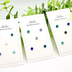 May include: Three cards displaying stud earrings in various colors, including blue, green, and silver. Each card has the text "Azalea Handmade Accessories". The earrings are small, round, and glittery, with a variety of shades.