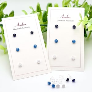 May include: Two cards with the text "Azalea Handmade Accessories" and a variety of blue and white glitter stud earrings.