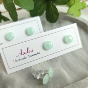 May include: Mint green stud earrings on white cards with the text "Azalea Handmade Accessories". The earrings are round and have a faceted texture. Additional earring backs are visible.