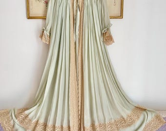 May include: A vintage light green robe with a delicate lace trim and accents. The robe features a collared neckline with a bow, long sleeves, and a flowing design. The lace trim is a soft beige color.
