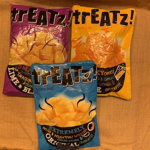 Può includere: Tre pochette con cerniera colorate con il testo "treatz!" e immagini di patatine fritte. Le pochette sono viola, gialle e blu.