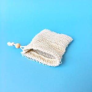 May include: A white mesh bag with a wooden bead drawstring. The bag is lying on a light blue background.