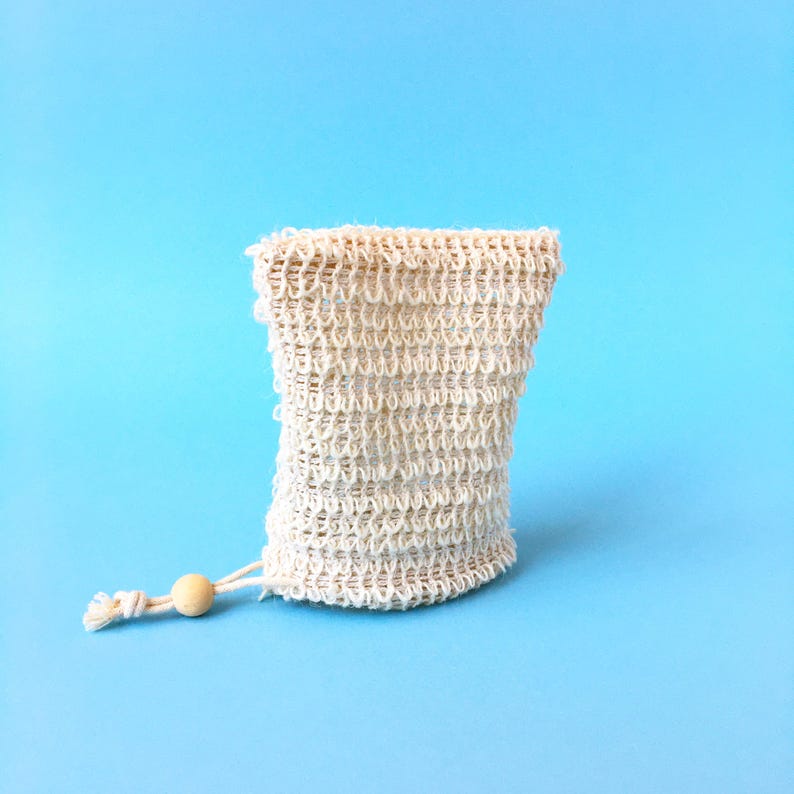 May include: A white mesh soap bag with a wooden bead on the drawstring. The bag is on a light blue background.