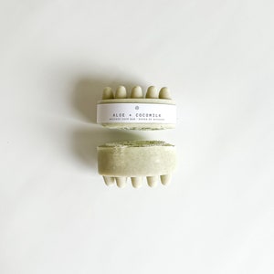 May include: A green massage soap bar with the text "ALOE + COCOMILK MASSAGE SOAP BAR - SAVON DE MASSAGE" on the label.