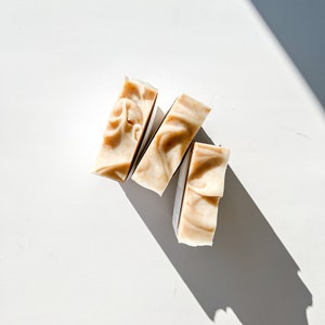 May include: Three bars of natural soap, each with a different swirl pattern, arranged in a triangular shape on a white background.