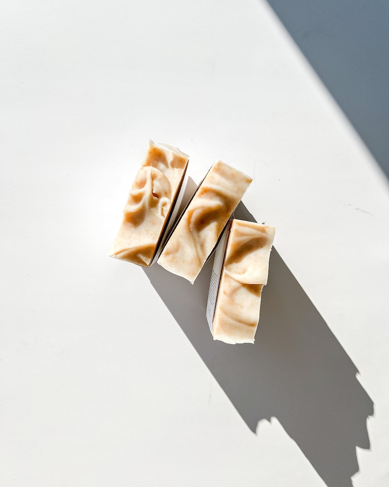 May include: Three bars of natural soap, each with a different swirl pattern, arranged in a triangular shape on a white background.
