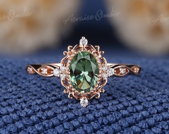 May include: A rose gold engagement ring with a green oval gemstone surrounded by smaller diamonds. The ring has a delicate, vintage-inspired design.