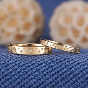 May include: Two gold wedding bands with a starburst design. The bands are stacked on top of each other.