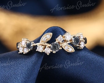 Op de afbeelding: Een delicate gouden ring met een bloemmotief met zwarte en witte diamanten. De ring ligt op een blauwe stoffen achtergrond.