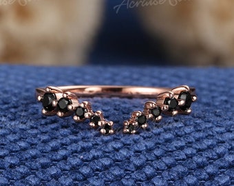 Op de afbeelding: Een delicate ring van roségoud met een gebogen ontwerp met zwarte edelstenen. De ring ligt op een blauwe stoffen achtergrond.