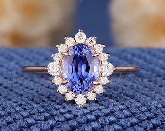 Op de afbeelding: Een verlovingsring van roségoud met een blauwe ovale saffier in het midden, omringd door een halo van kleinere diamanten.