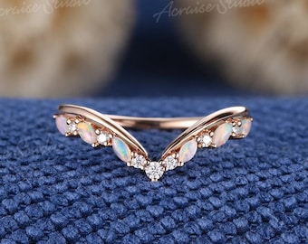 May include: A delicate rose gold ring with a V-shaped design. The ring is adorned with small, round diamonds and oval-shaped opals.