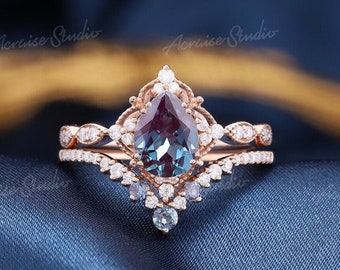 May include: A pear-shaped, dark blue gemstone ring with a rose gold setting and a delicate band. The ring is surrounded by smaller diamonds and has a vintage-inspired design.
