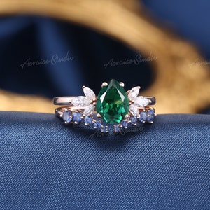 May include: A pear-shaped emerald green gemstone ring with a halo of smaller diamonds and a matching band with blue sapphires.
