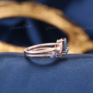 May include: A rose gold ring set with a large oval blue gemstone surrounded by smaller white gemstones. The band is adorned with smaller blue gemstones.