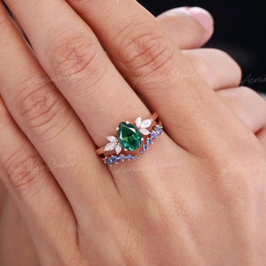 May include: A pear-shaped green gemstone engagement ring with a delicate floral design and a matching band of blue gemstones.