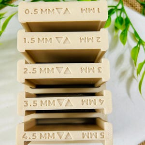 May include: A stack of beige, rectangular tools with measurements etched on them. The tools are labeled with sizes ranging from 0.5 MM to 4.5 MM. The tools are stacked on top of each other.