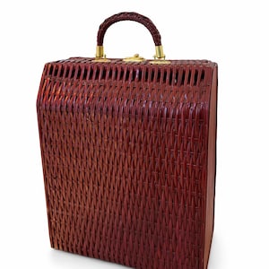 May include: A vintage, rectangular, woven wicker handbag in a rich, reddish-brown hue. It features a braided handle, brass-toned hardware, and a secure clasp. The bag's design showcases a classic, structured silhouette, ideal for carrying essentials.