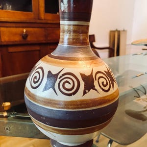 May include: A brown and white ceramic vase with a geometric design. The vase has a round body and a narrow neck.