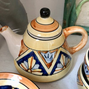 May include: A yellow teapot with a brown lid and handle, decorated with blue, brown, and white geometric patterns. The teapot is part of a tea set.