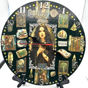 May include: Circular, dark green clock with a black stand. The clock face features a central image of a woman, surrounded by tarot-style illustrations and the word "Wicca". Gold accents and black clock hands complete the design.