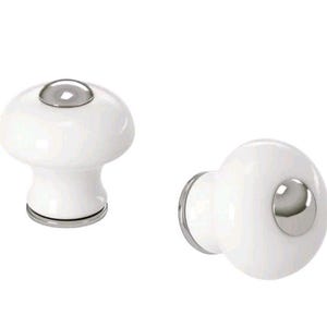 May include: Two white ceramic cabinet knobs with a mushroom-like shape. Each knob features a silver-colored metal accent on the top and base. The knobs are designed for furniture and home decor.