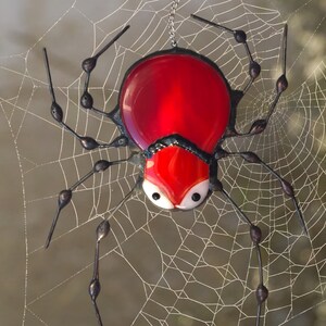 May include: A red glass spider with black legs and black accents hanging in a spider web.