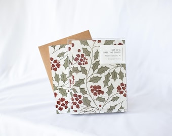 May include: A set of six greeting cards in a clear plastic sleeve with a brown envelope. The cards feature a repeating pattern of dark red berries and sage green holly leaves on a white background. A white label reads SET OF 6 GREETING CARDS.