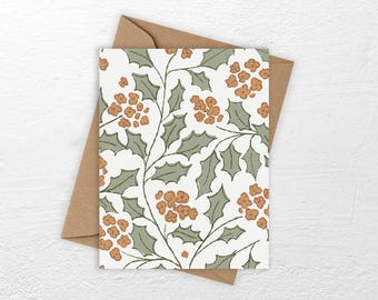 May include: A rectangular greeting card featuring a repeating botanical pattern of sage green holly leaves and clusters of small orange berries on a white background, placed on top of a plain brown paper envelope.