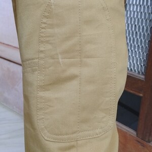 May include: A pair of khaki pants with a reinforced knee patch. The patch is sewn with a decorative stitch.