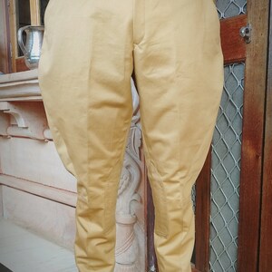 May include: A pair of tan riding pants with a slight flare at the bottom. The pants have a belt loop and a button closure.