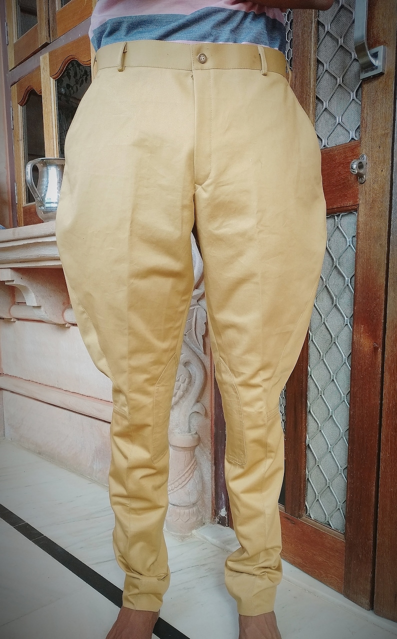 May include: A pair of tan riding pants with a slight flare at the bottom. The pants have a belt loop and a button closure.