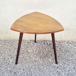 May include: A mid-century style side table with a triangular top and three dark brown legs. The tabletop is made of light-coloured wood. The table is approximately 61 cm wide.