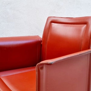 May include: A red leather armchair with a high back and a curved armrest. The chair has a simple, modern design.