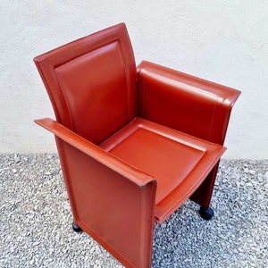 May include: A red leather armchair with a square seat and a high back. The chair has a modern design and is on wheels.