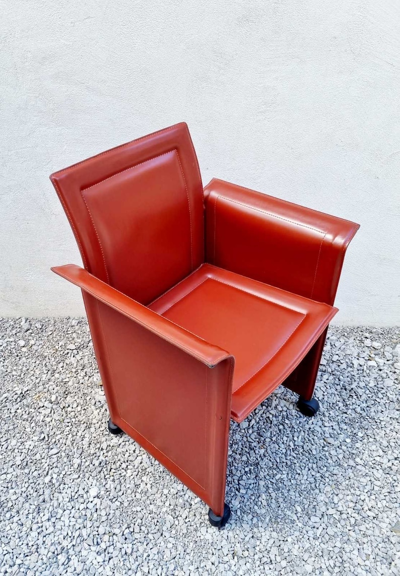 May include: A red leather armchair with a square seat and a high back. The chair has a modern design and is on wheels.