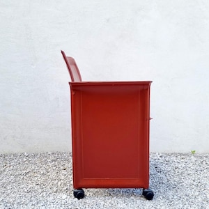 May include: A red rolling cabinet with three drawers and black wheels. The cabinet is made of metal and has a sleek, modern design.